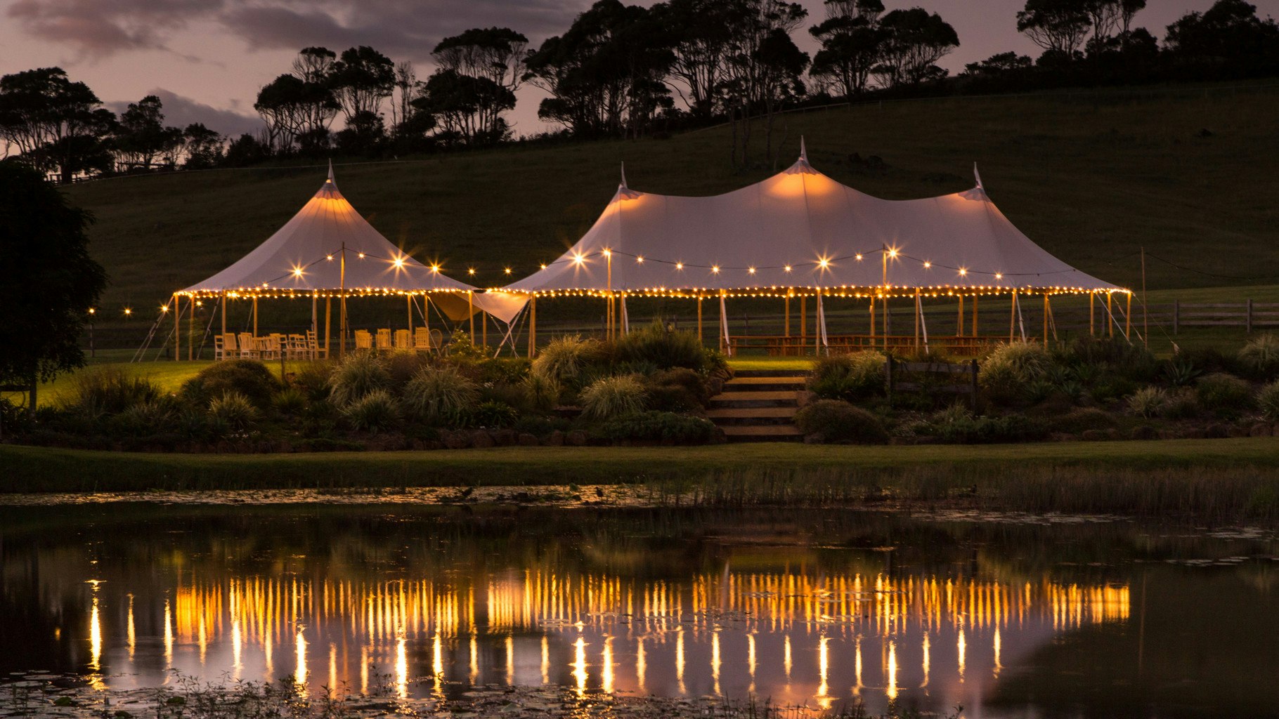 Tipi lit up at night with lights shining in water reflection.